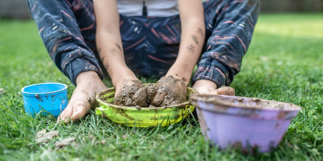 Child sat on grass, playing with mud in bowls