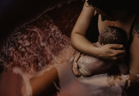 A new mother cradles her newborn in a birthing pool, surrounded by soft, warm water, capturing an intimate moment of early bonding.